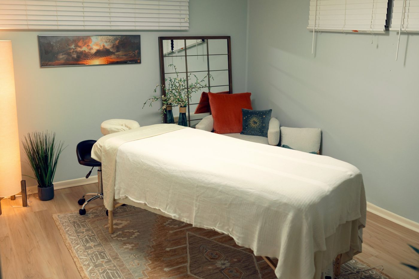 The treatment room: a draped massage table, a lamp, and a reading chair with a rust-colored pillow